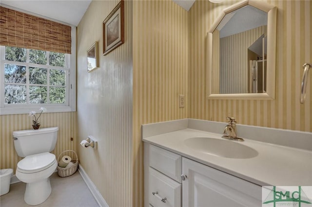 bathroom with toilet, wallpapered walls, baseboards, and vanity