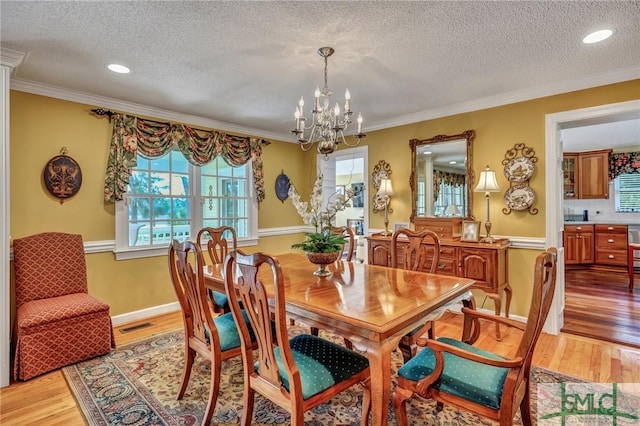 dining area featuring light wood finished floors, visible vents, ornamental molding, a textured ceiling, and a chandelier