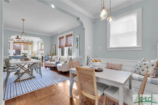 dining space featuring arched walkways, breakfast area, wood finished floors, and ornamental molding