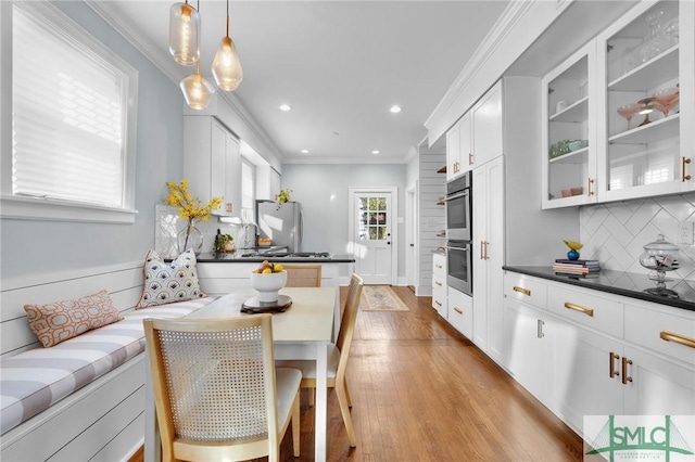 kitchen featuring stainless steel appliances, white cabinetry, dark countertops, glass insert cabinets, and pendant lighting