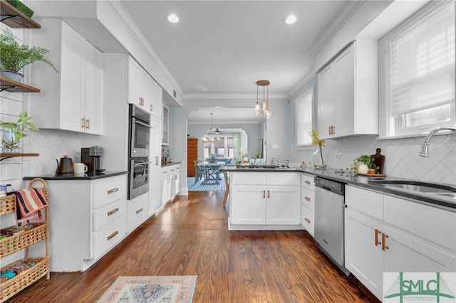 kitchen with stainless steel appliances, a peninsula, a sink, white cabinets, and dark countertops