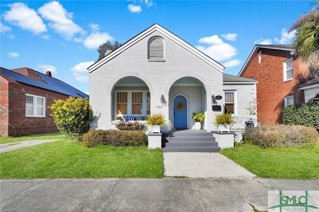 view of front of property featuring covered porch, brick siding, and a front lawn