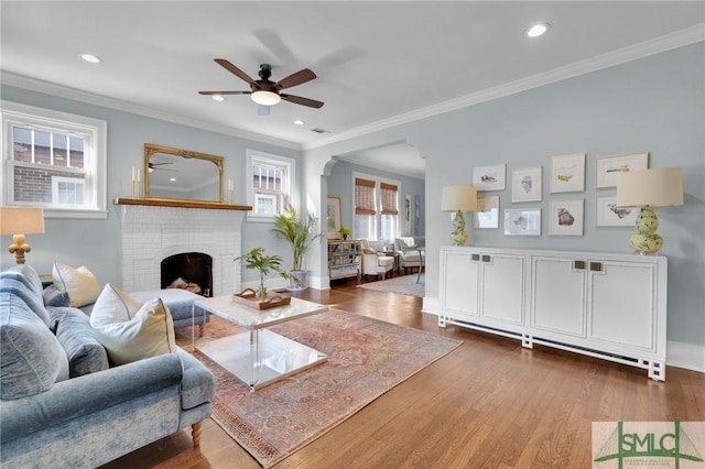 living area with dark wood-style floors, ornamental molding, a brick fireplace, and visible vents