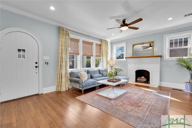 living area featuring baseboards, a fireplace, ornamental molding, and wood finished floors