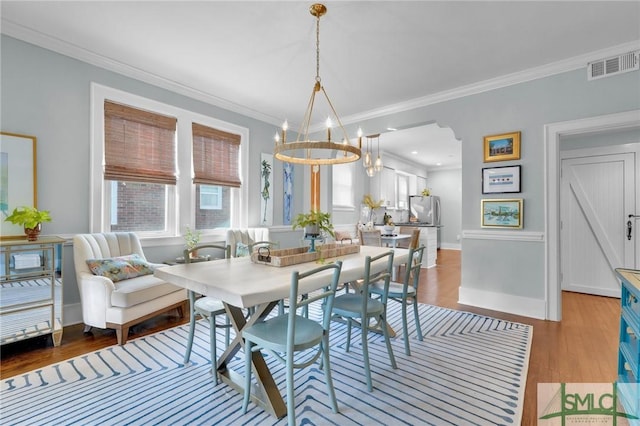 dining area with light wood-style floors, visible vents, an inviting chandelier, and ornamental molding