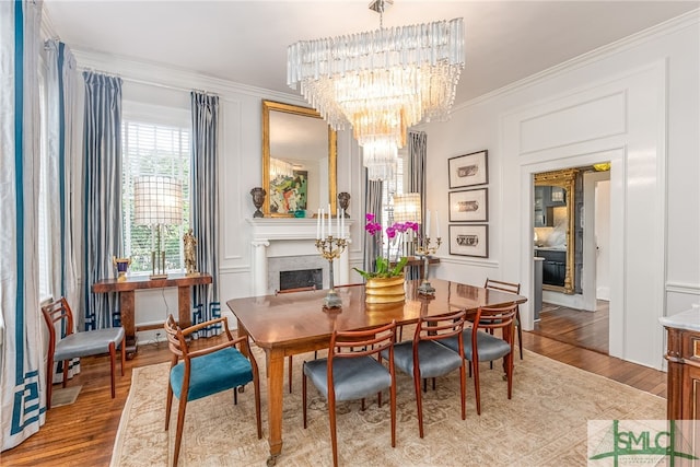 dining area with a fireplace, a decorative wall, an inviting chandelier, ornamental molding, and light wood-type flooring