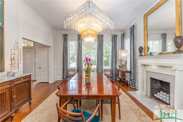 dining space featuring crown molding, a fireplace with flush hearth, light wood-style flooring, and a notable chandelier