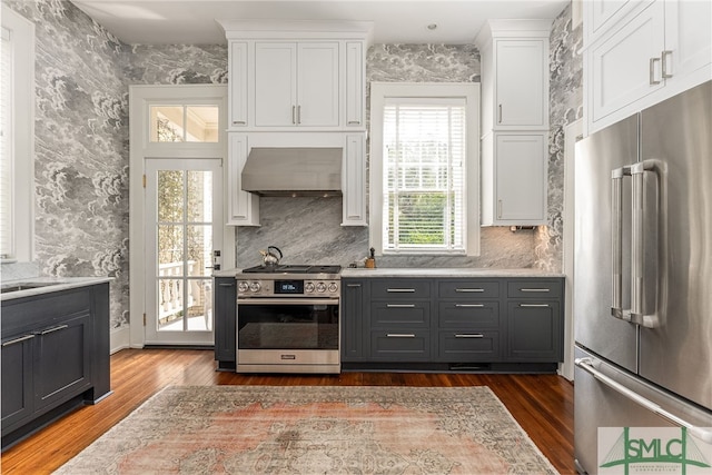 kitchen with white cabinetry, appliances with stainless steel finishes, range hood, dark wood-style floors, and wallpapered walls