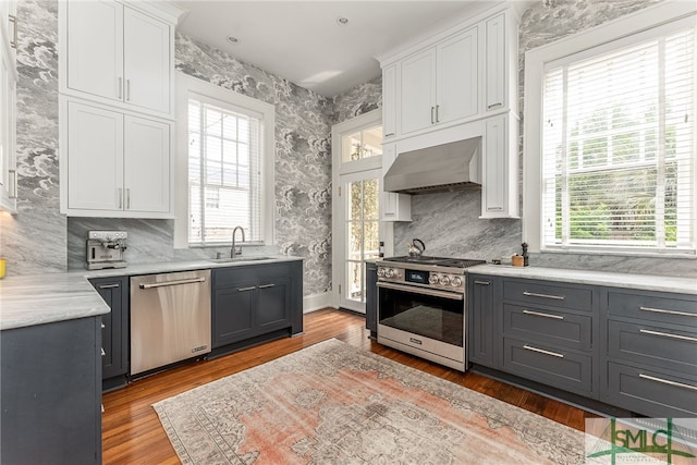 kitchen featuring stainless steel appliances, range hood, white cabinets, and wallpapered walls