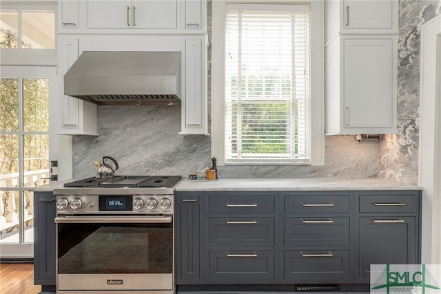 kitchen with stainless steel range oven, wall chimney range hood, gray cabinets, and white cabinetry