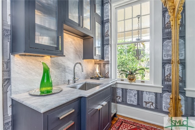 kitchen with light countertops, backsplash, a sink, and glass insert cabinets