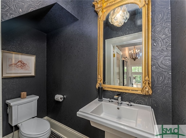 half bath featuring wallpapered walls, baseboards, toilet, a chandelier, and a sink