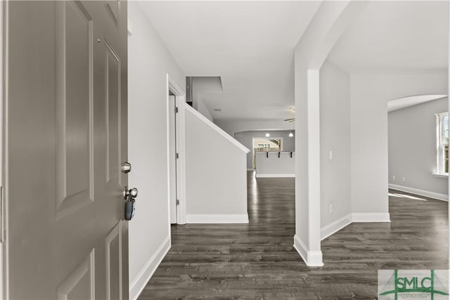 entryway with arched walkways, dark wood-type flooring, and baseboards