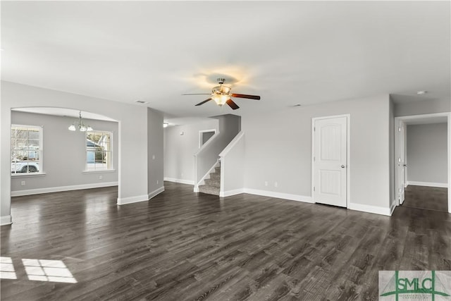 unfurnished living room with dark wood-style floors, baseboards, stairway, and ceiling fan with notable chandelier