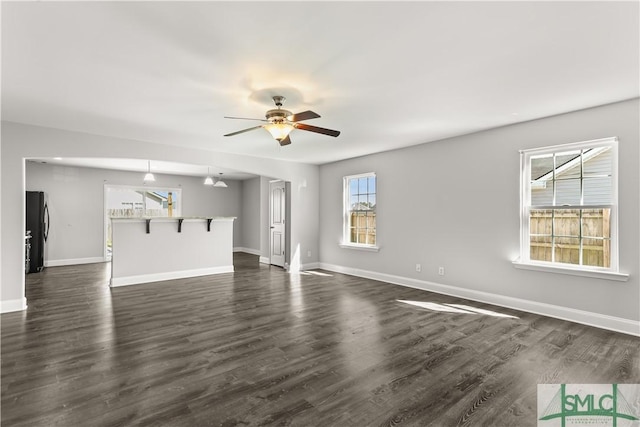 unfurnished living room with dark wood-style floors, ceiling fan, and baseboards