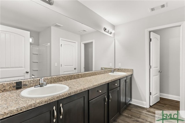 full bath with double vanity, visible vents, a sink, and wood finished floors