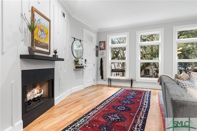 interior space featuring ornamental molding, visible vents, a lit fireplace, and wood finished floors