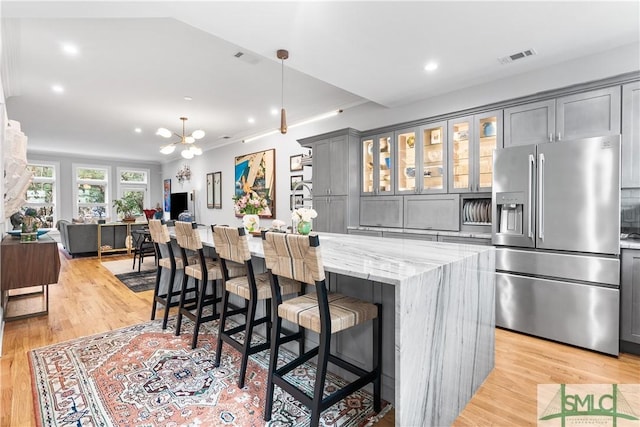 kitchen with light stone counters, a center island, gray cabinets, light wood-style floors, and stainless steel fridge