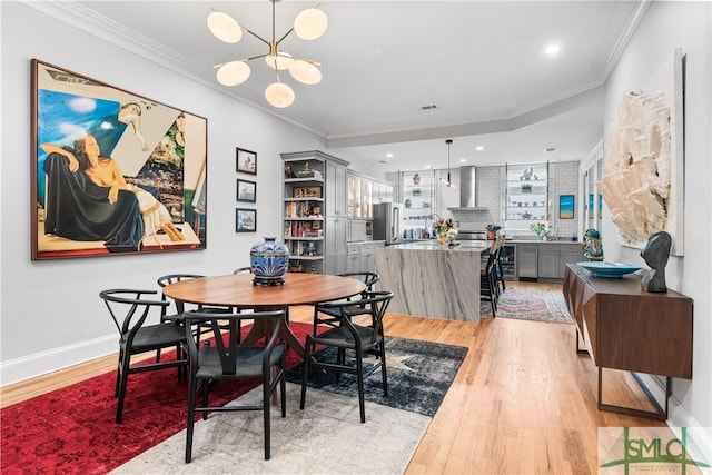 dining area featuring a chandelier, ornamental molding, light wood-style flooring, and baseboards