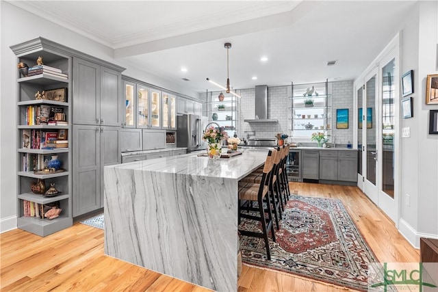 kitchen with open shelves, gray cabinets, wall chimney range hood, beverage cooler, and stainless steel fridge