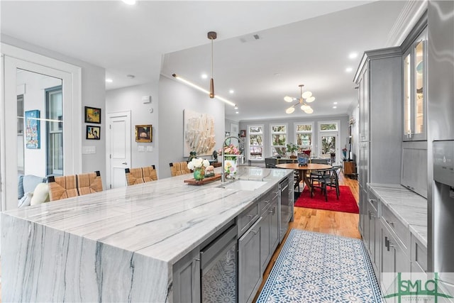 kitchen featuring a notable chandelier, gray cabinetry, a sink, light stone countertops, and a large island with sink