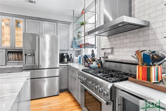 kitchen with appliances with stainless steel finishes, gray cabinets, wall chimney range hood, and backsplash