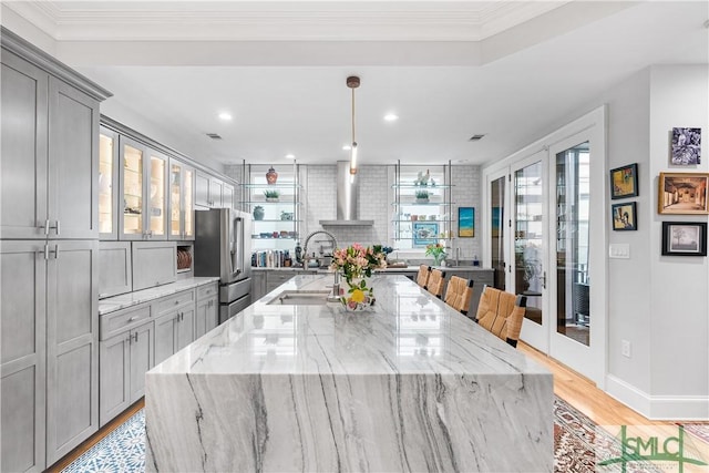 kitchen with light wood finished floors, high end refrigerator, a wood stove, gray cabinetry, and a sink