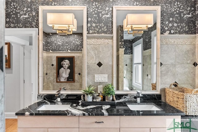 bathroom with double vanity, wallpapered walls, and a sink