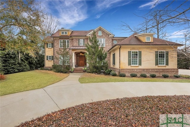 view of front facade with a front yard, brick siding, and stucco siding