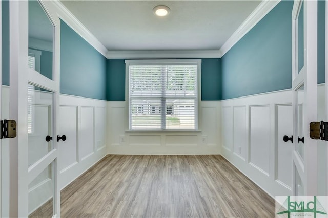 empty room featuring crown molding, a wainscoted wall, a decorative wall, and wood finished floors