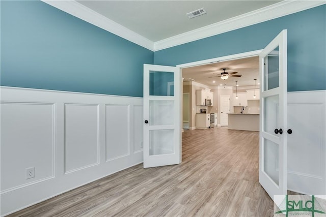 spare room with a decorative wall, visible vents, light wood-style floors, ornamental molding, and french doors