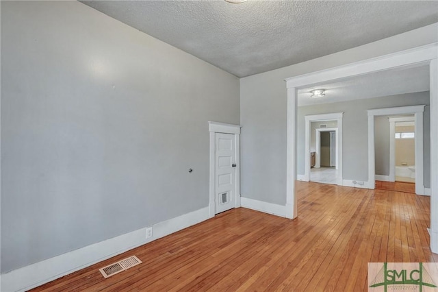 spare room with light wood-style floors, baseboards, visible vents, and a textured ceiling