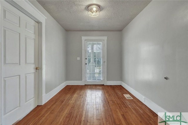 doorway featuring baseboards, visible vents, a textured ceiling, and hardwood / wood-style floors