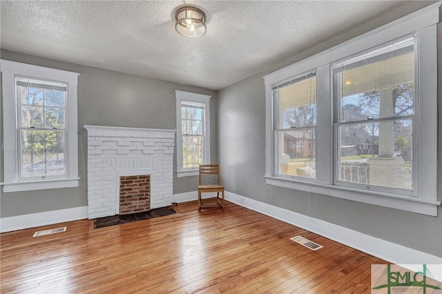 unfurnished living room featuring a brick fireplace, wood-type flooring, visible vents, and baseboards