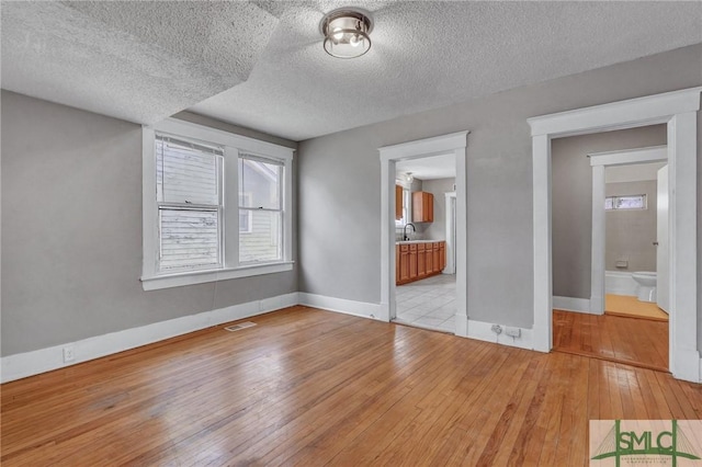 interior space featuring light wood-style floors, baseboards, multiple windows, and visible vents