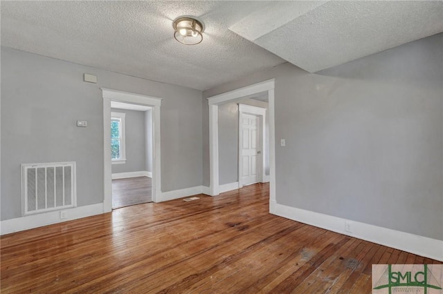 empty room featuring a textured ceiling, wood-type flooring, visible vents, and baseboards