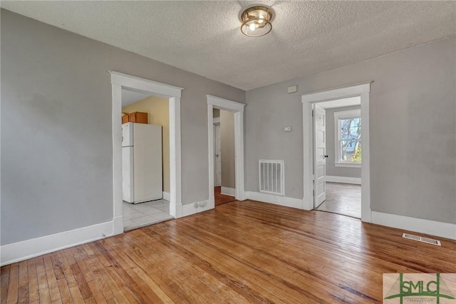 empty room with light wood-style floors, visible vents, and baseboards