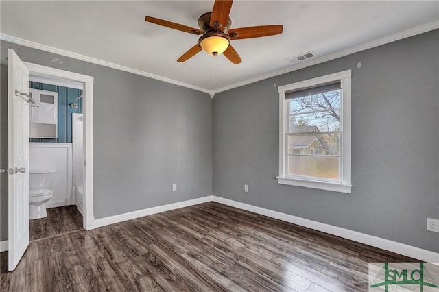 unfurnished bedroom featuring baseboards, visible vents, dark wood-style flooring, ensuite bathroom, and crown molding