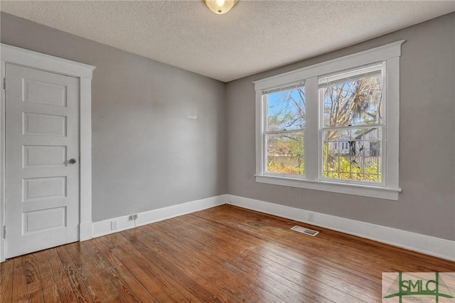 empty room with a textured ceiling, wood-type flooring, visible vents, and baseboards