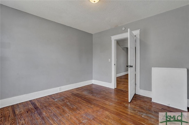 spare room with a textured ceiling, hardwood / wood-style flooring, and baseboards