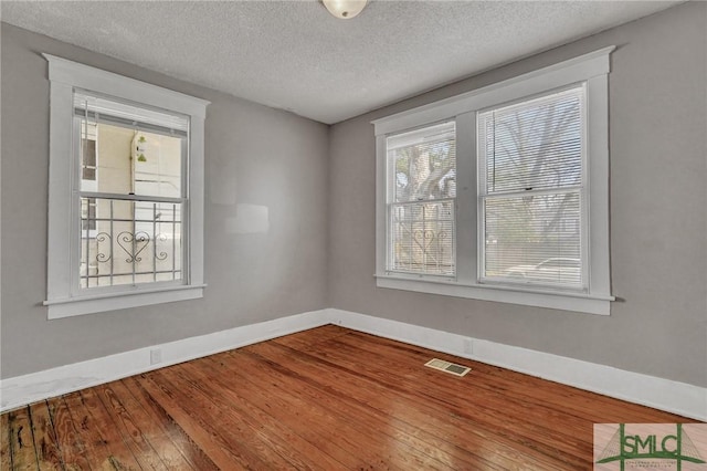 unfurnished room with a textured ceiling, wood-type flooring, visible vents, and baseboards