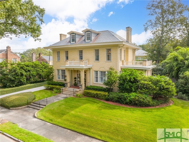 colonial-style house featuring a front lawn, a high end roof, and a balcony