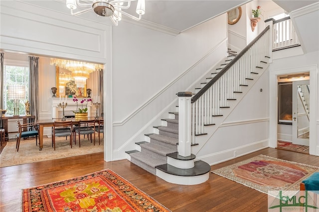 stairway with a notable chandelier, a decorative wall, wood finished floors, and crown molding