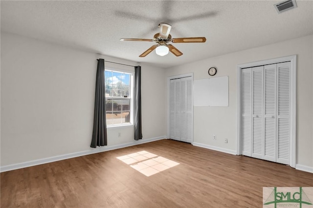 unfurnished bedroom featuring baseboards, visible vents, multiple closets, and wood finished floors