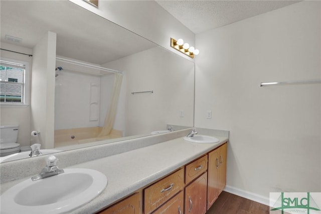 full bathroom with toilet, double vanity, a textured ceiling, and a sink