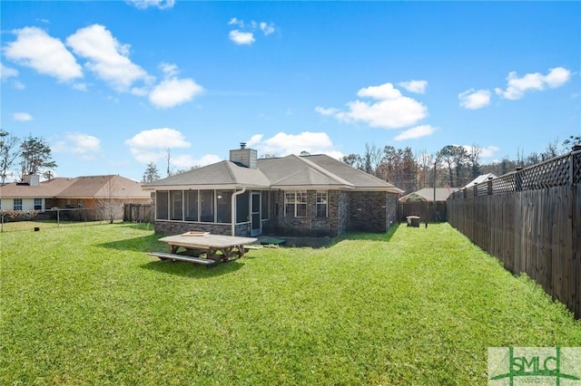 back of house with a lawn, a chimney, a fenced backyard, and a sunroom