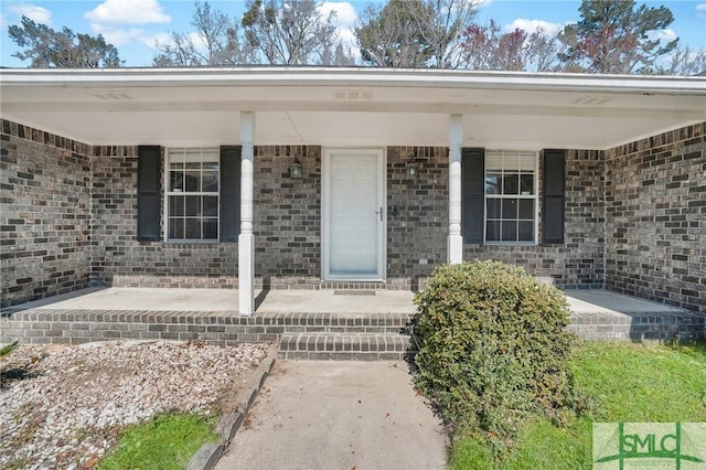 view of exterior entry with a porch and brick siding