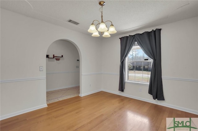 empty room with arched walkways, a textured ceiling, wood finished floors, visible vents, and an inviting chandelier