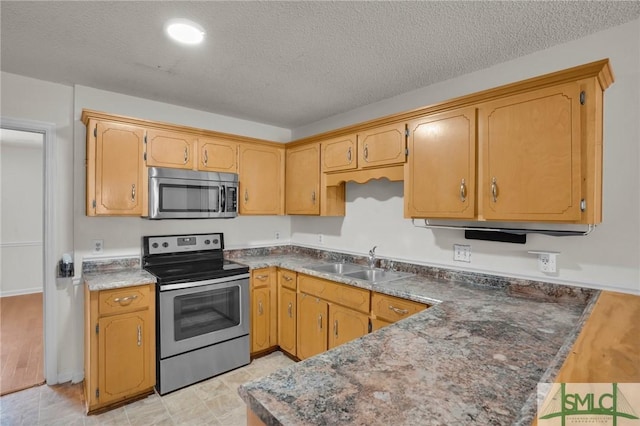 kitchen with dark countertops, a peninsula, stainless steel appliances, a textured ceiling, and a sink