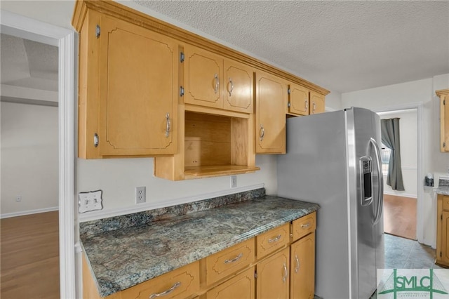 kitchen featuring baseboards, stainless steel refrigerator with ice dispenser, and a textured ceiling